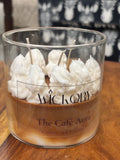 Close-up of a Wickory handcrafted beeswax candle labeled “The Café Aura – Coffee and Caramel,” featuring layered caramel-brown and ivory wax topped with piped white wax resembling whipped cream inside a clear glass jar.
