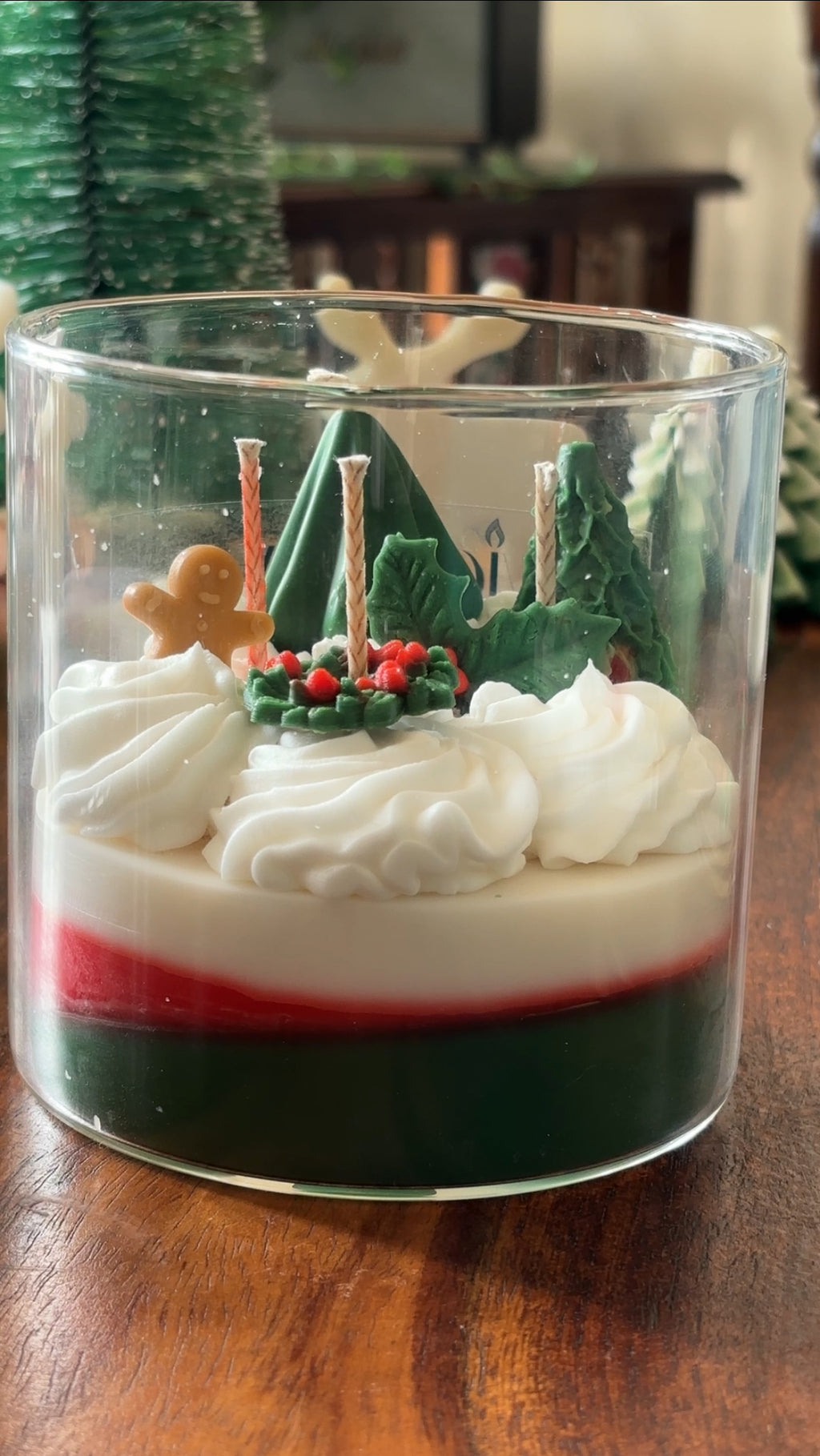 Lifestyle shot of Wickory The Snowy Spruce handcrafted layered beeswax candle in a clear glass jar, featuring festive green, red and white wax layers with sculpted gingerbread, holly and tree details