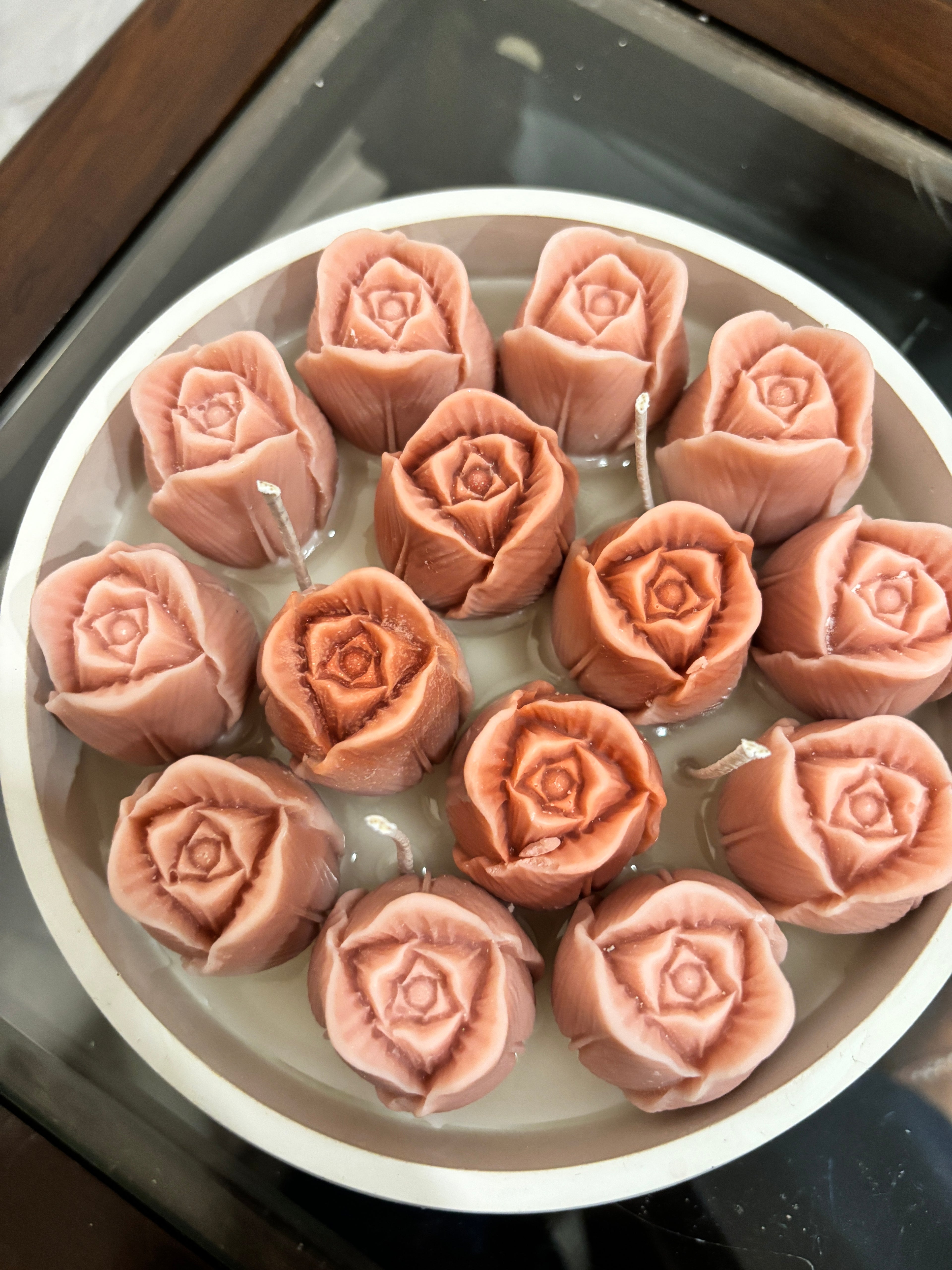 A handcrafted beeswax candle in a wide white bowl, filled with multiple sculpted blush-pink rose-shaped beeswax blooms and cotton wicks, arranged closely together for a lush, floral look.