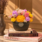 The Blossom Garden: a multicolour sculpted candle flower bouquet in a dark ribbed pot, on a stack of books
