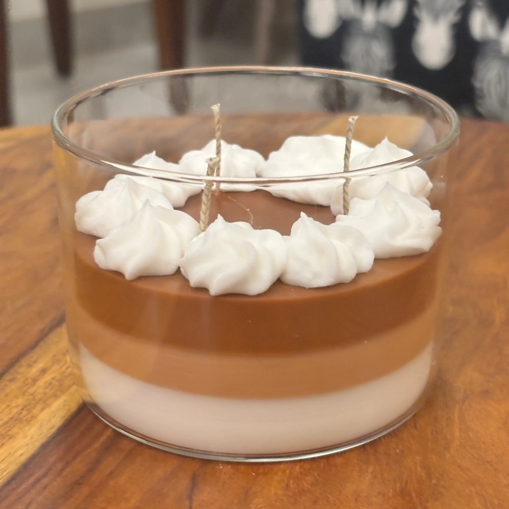 The Café Aura coffee-inspired candle in a glass jar with layered coffee-colored wax and whipped cream topping