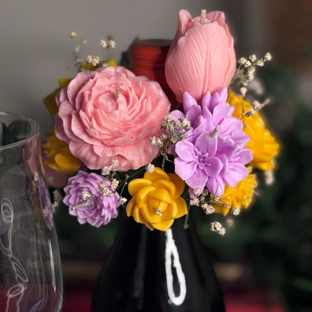 Close-up of Cork & Bloom: hand-sculpted beeswax pink rose, tulip, lilac and yellow flowers with baby's breath around the neck of a black wine bottle