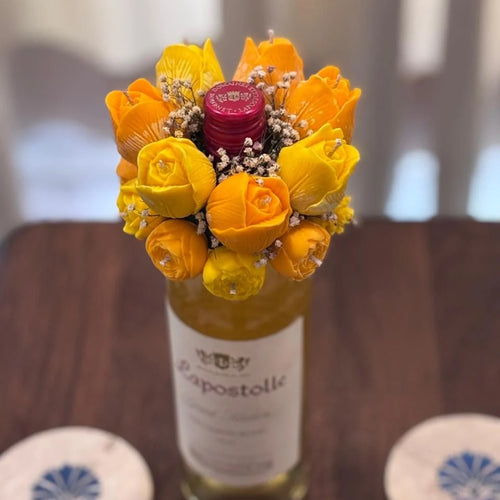Cork & Bloom beeswax flower candle topper in yellow and orange roses with baby's breath, on a wine bottle on a wooden table