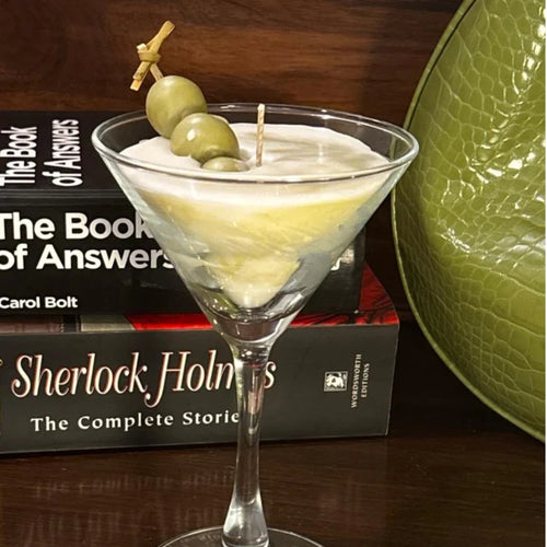 Dirty Martini candle with olives on a skewer, styled beside a stack of books