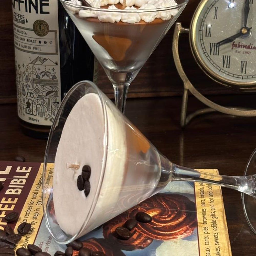 Espresso Martini candles styled with coffee beans, a coffee book and a vintage clock, one glass tipped to show the creamy top