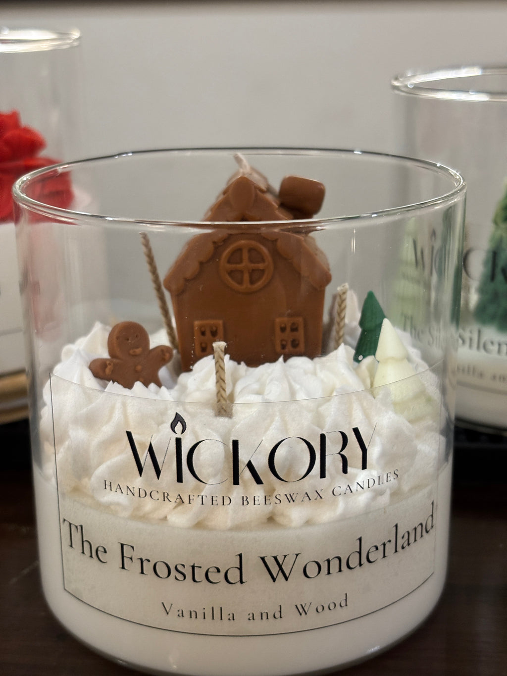 The Frosted Wonderland Wickory beeswax candle in a labelled glass jar: sculpted gingerbread house, gingerbread figure and small trees on whipped white wax