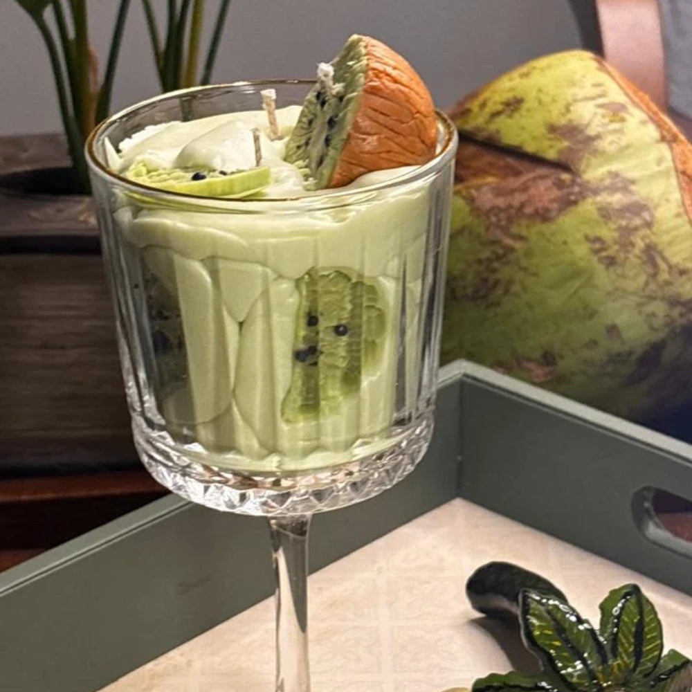 Kiwi Colada candle styled with a coconut on a tray, kiwi slices pressed against the glass