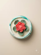 Lotus Still, top view: sculpted coral-pink lotus and green leaves in a wide marbled teal and white bowl