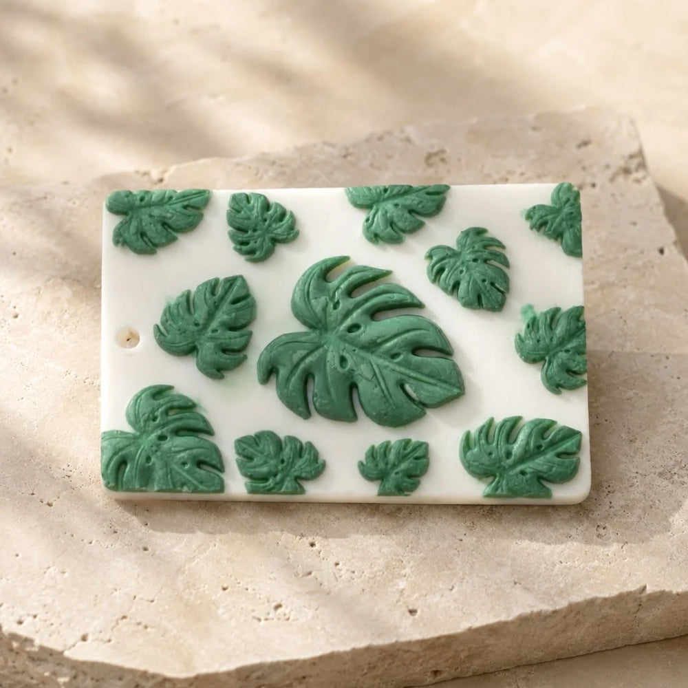 Monstera wax sachet with sculpted green monstera leaves, resting on a textured stone slab