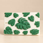 Wickory Monstera wax sachet: scattered sculpted green monstera leaves on an ivory beeswax tile