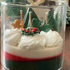 Close-up of The Snowy Spruce: green and red wax layers under whipped white wax, sculpted pine trees, holly, berries and a gingerbread figure