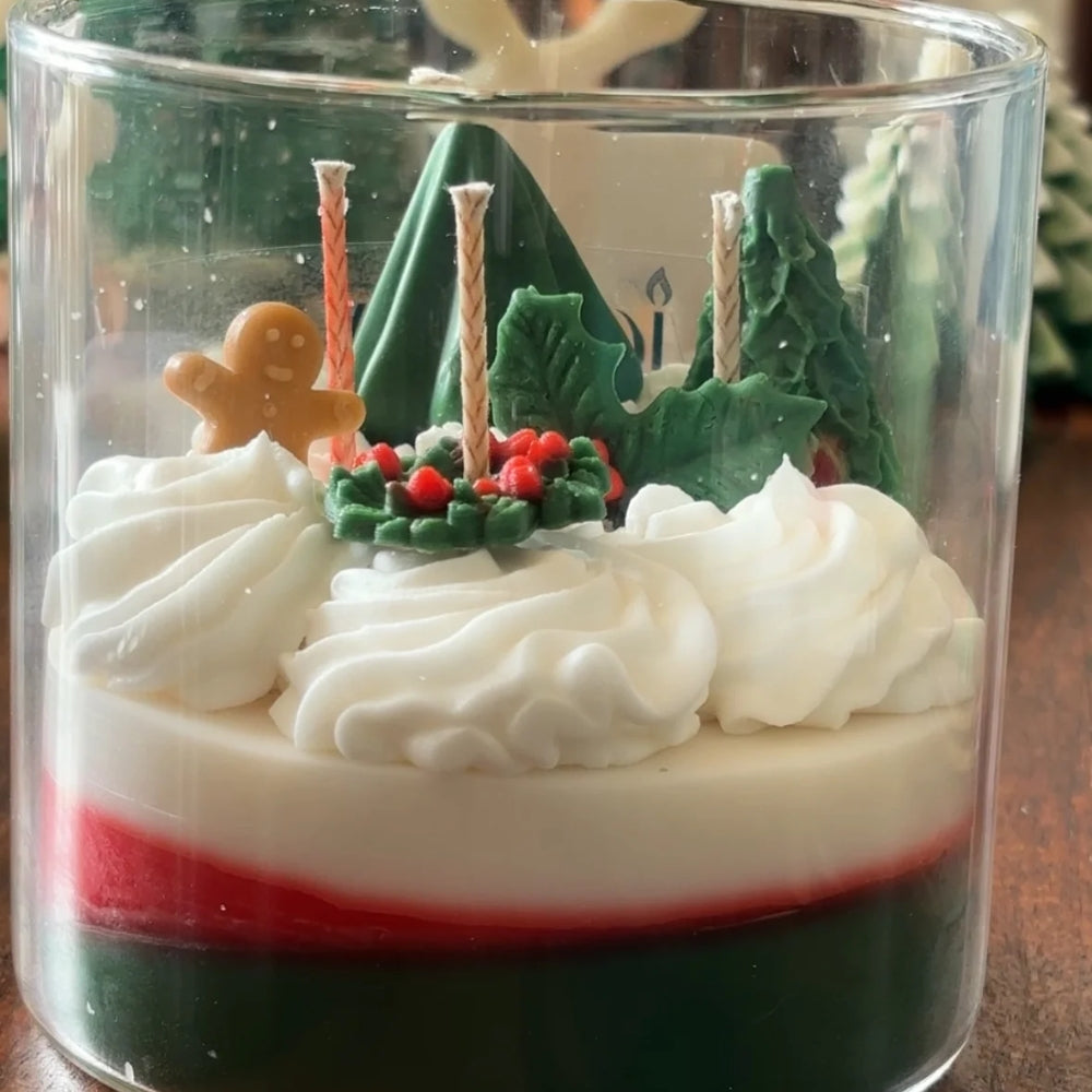 Close-up of The Snowy Spruce: green and red wax layers under whipped white wax, sculpted pine trees, holly, berries and a gingerbread figure