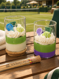 Wickory Tennis Candle: two glass jar candles in green-and-ivory and green-and-purple layers, topped with whipped wax, sculpted tennis balls and racquets, beside a tennis court