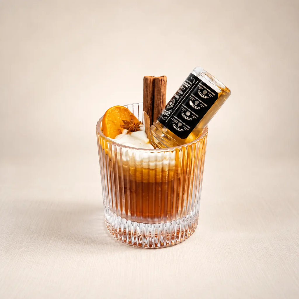Whiskey Sour beeswax candle: amber wax and a foam top in a ribbed rocks glass, with an orange slice, cinnamon stick and mini bottle